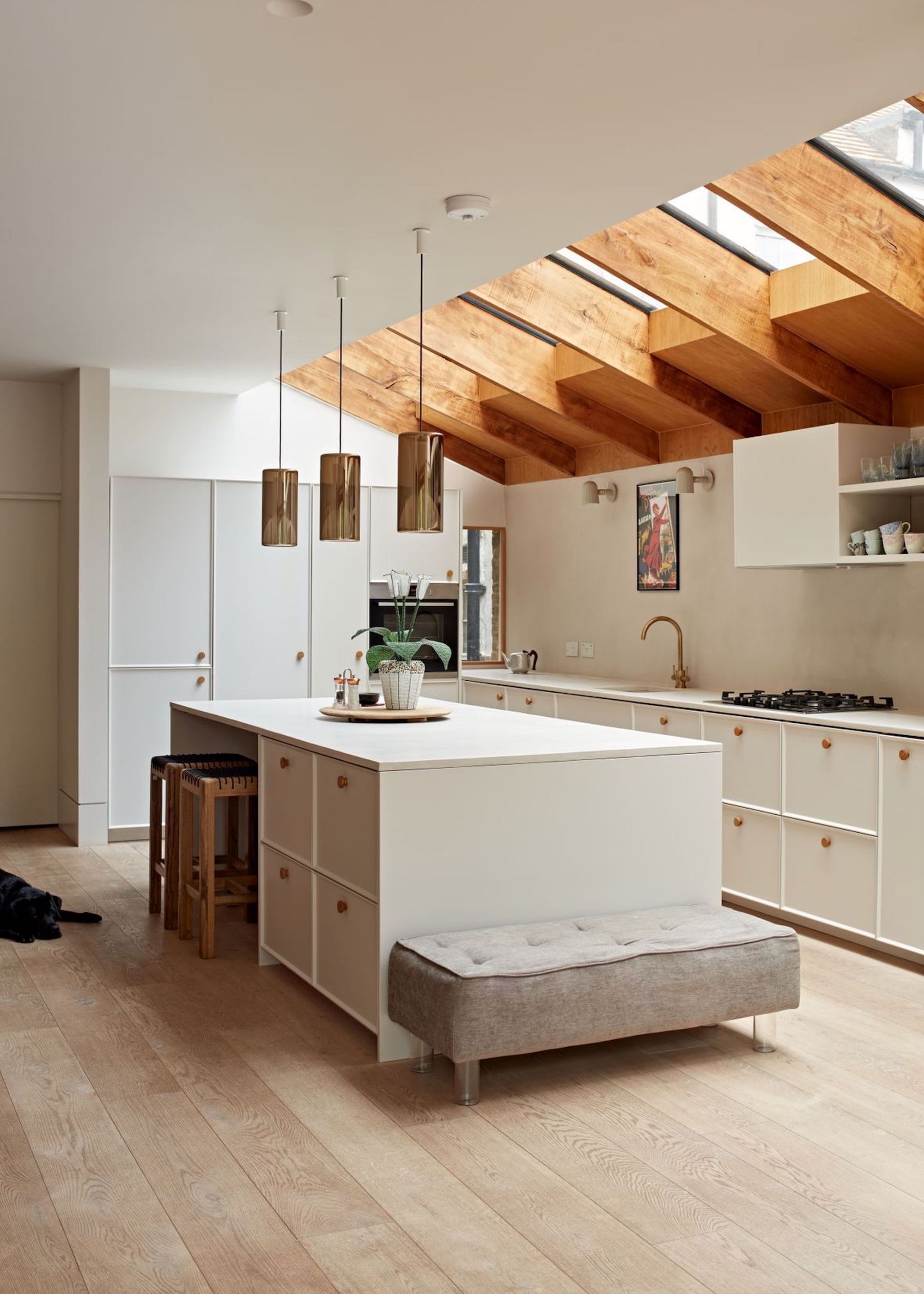 A kitchen extension with a white island that has extra storage inside, as well as kitchen cabinets, a stove, and a sink. Above the island are three pendant lights.