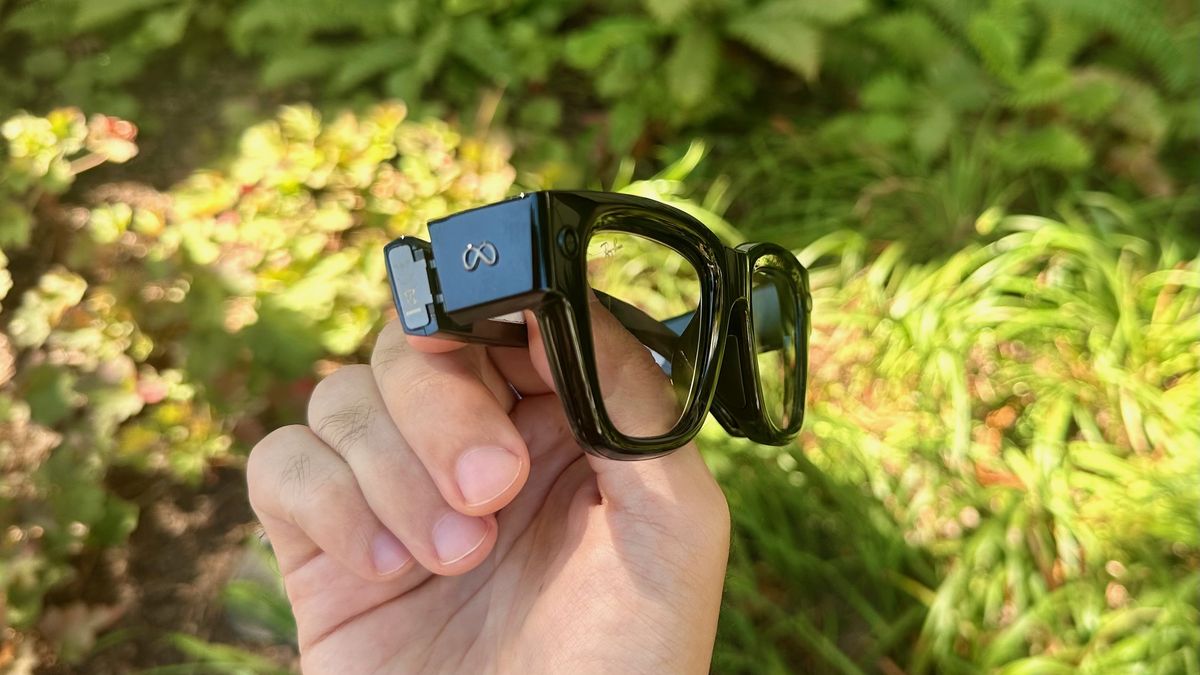 A close-up of the Meta Ray-Ban Display glasses held in hand from a side view showing the Meta logo and the thickness of the frames.