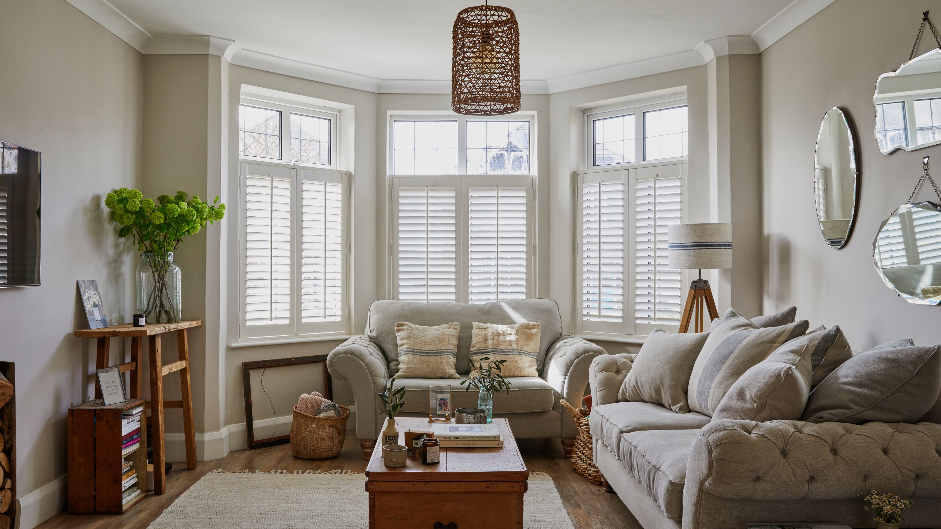 Neutral living room with light grey sofa and snuggle chair, wooden coffee table and white shutters on the bay window