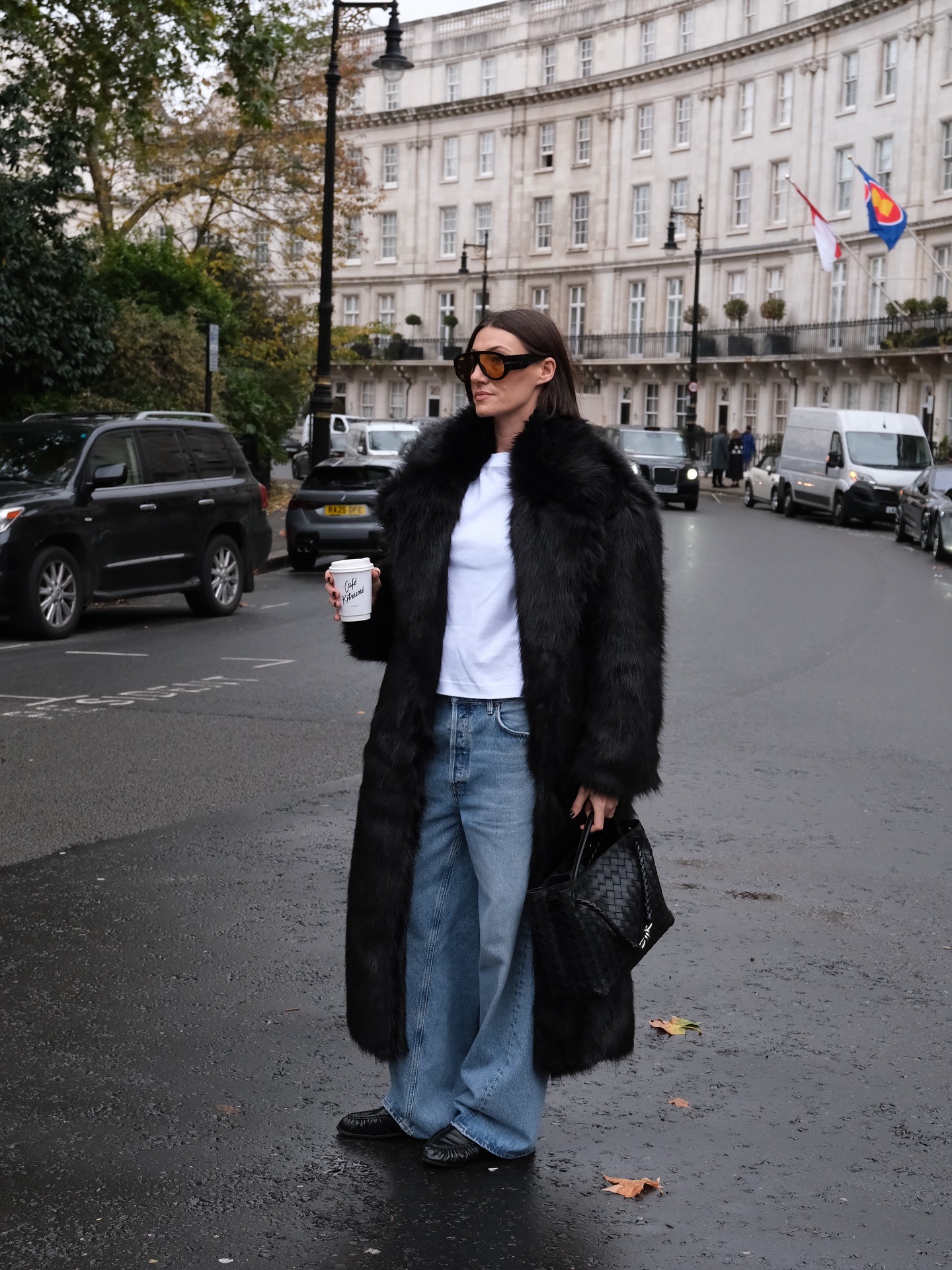 Sarah wears a black fur coat, white tee, baggy jeans, loafers, and a Bottega Veneta bag.