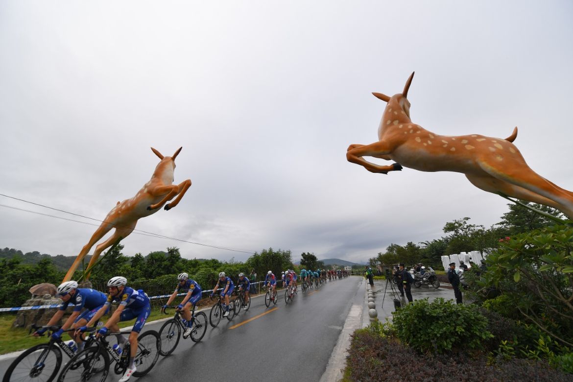 The peloton passes under two roadside figurines