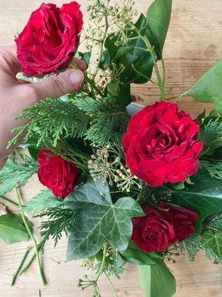 Christmas table centerpiece step by step, placing roses between the foliage in the bowl