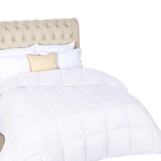 A white comforter on a bed with a beige padded headboard and matching cushion with white pillows