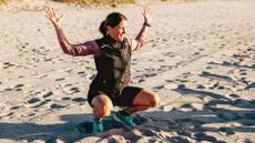 Woman at the bottom of a squat with hands in the air on the beach
