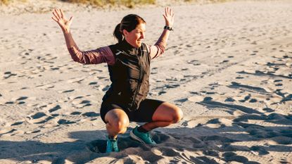 Woman at the bottom of a squat with hands in the air on the beach