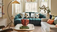 neutral living room with a traditional bay window with cafe curtains. A curved textured sofa in teal sits in the window with a cord and linen neutral couch with a curved freestanding lamp