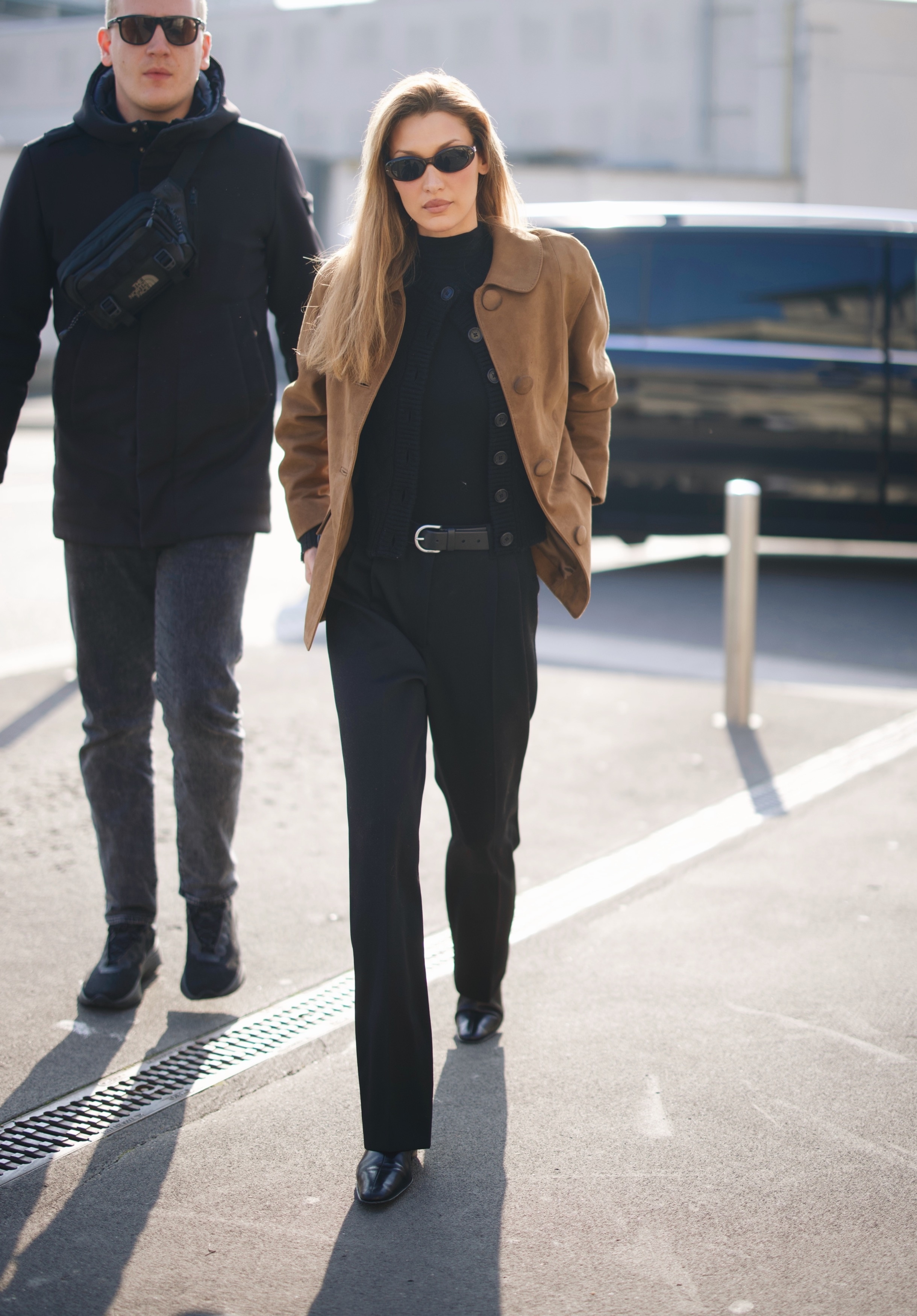 Bella Hadid wears back trousers with black almond-toe boots and suede jacket.