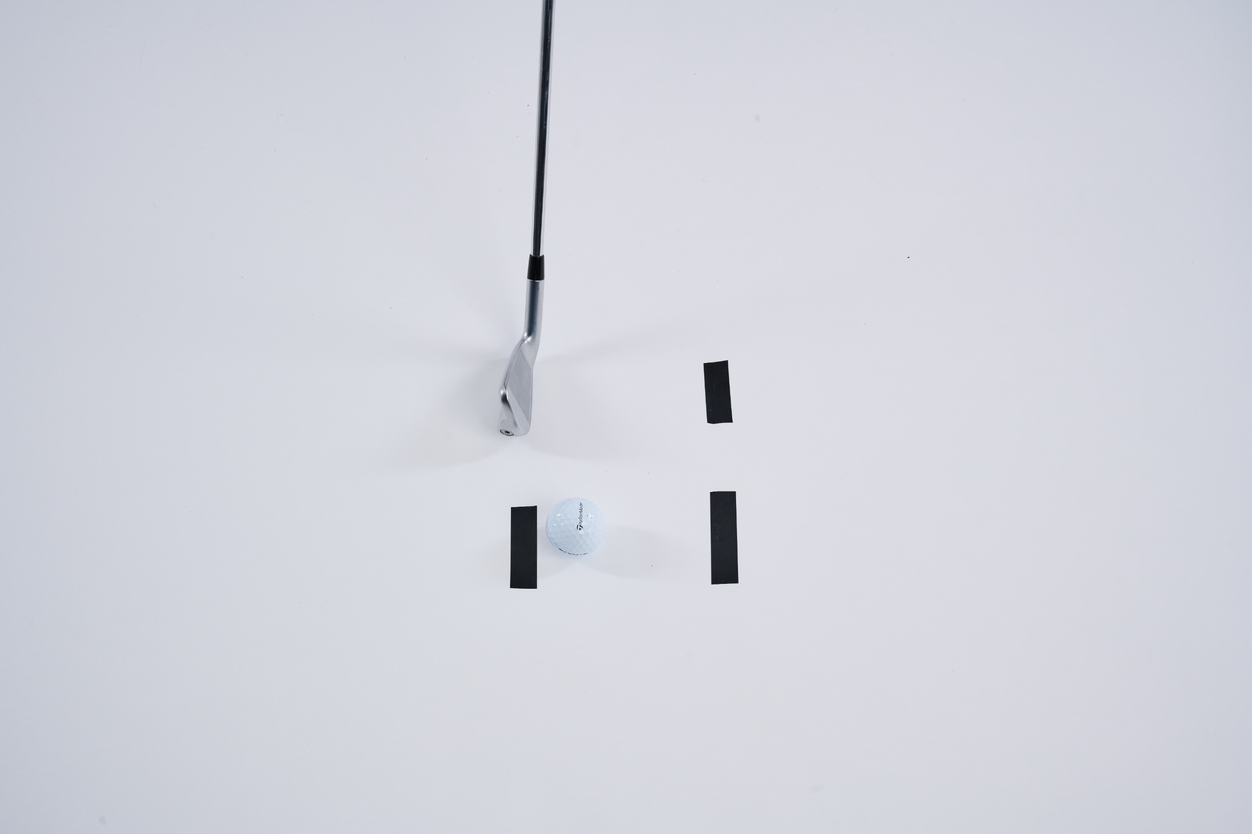 A golf club set behind a piece of tape on the ground, with two pieces of tape outside the club path to the right