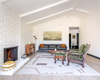 White living room with velour green upholstery on wooden armchair and painting on the back wall above dark leather couch