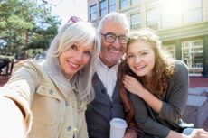 Attractive grandparents smile with their granddaughter outside. The granddather holds a coffee cup.