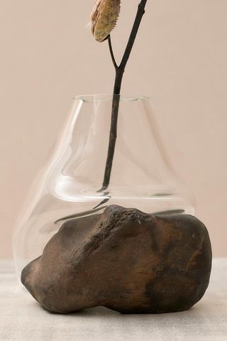A clear glass vase that's blown around the rock in copper tones. There are tree branches in the vase.