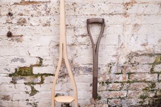 A one piece 'Y' shaped step ladder leaning against a brick wall next to a spade.