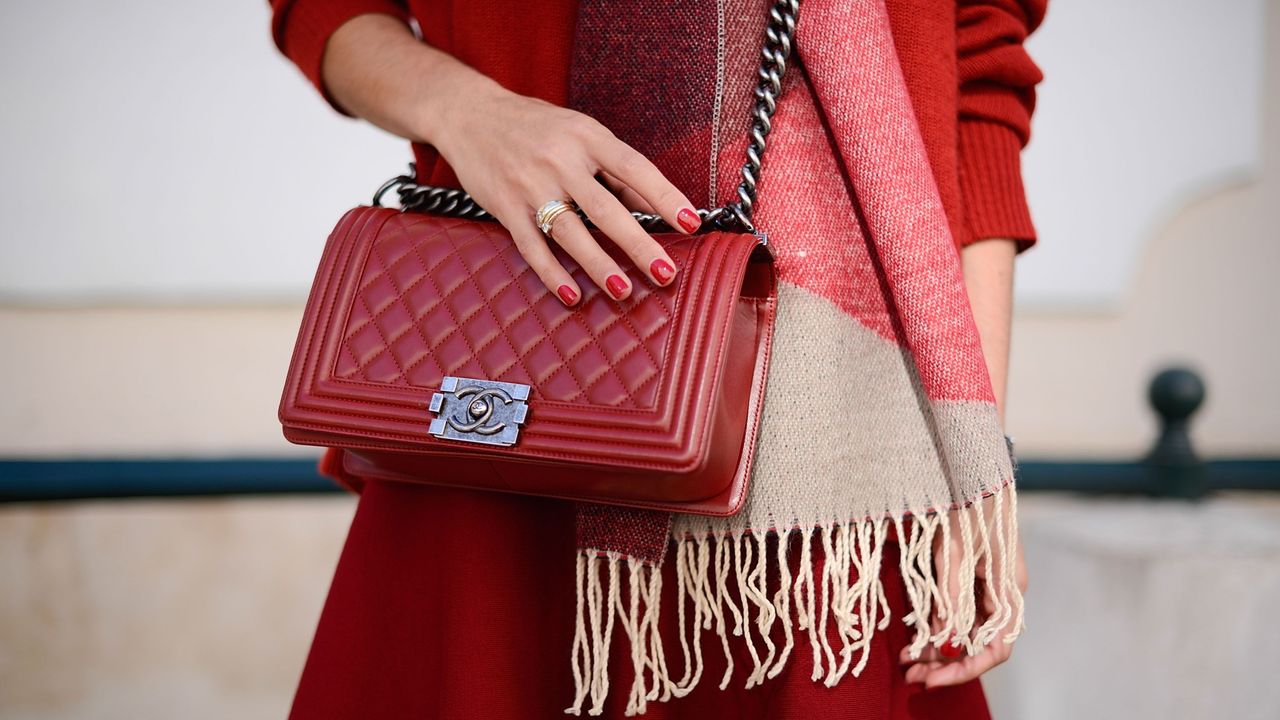 women with shiny red nails and thick ring holds a bag