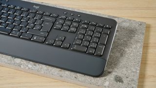 a black full sized keyboard with batteries and a palm rest on a clean beige surface with a blue backdrop