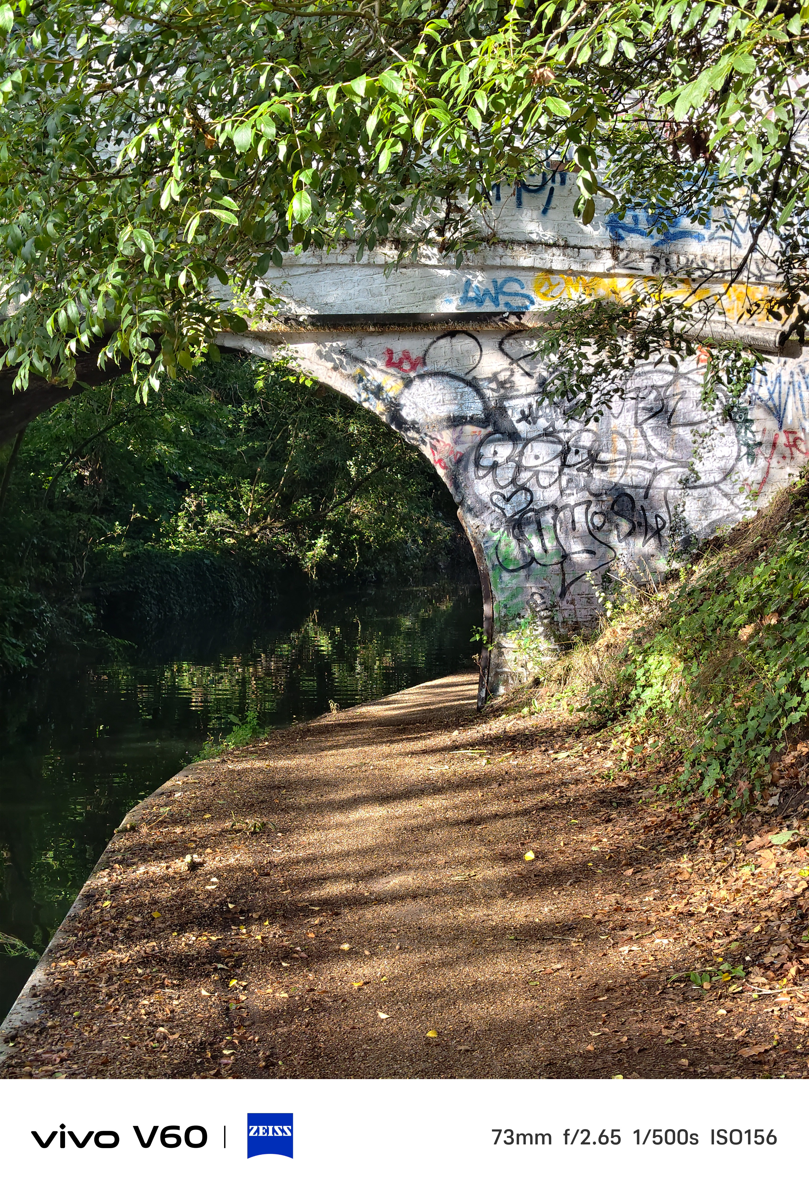 A canal path leading under a bridge covered in graffiti