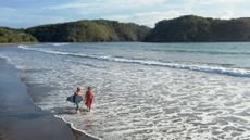 Aerial view of a mature couple carrying a surfboard along the water's edge in Panama.