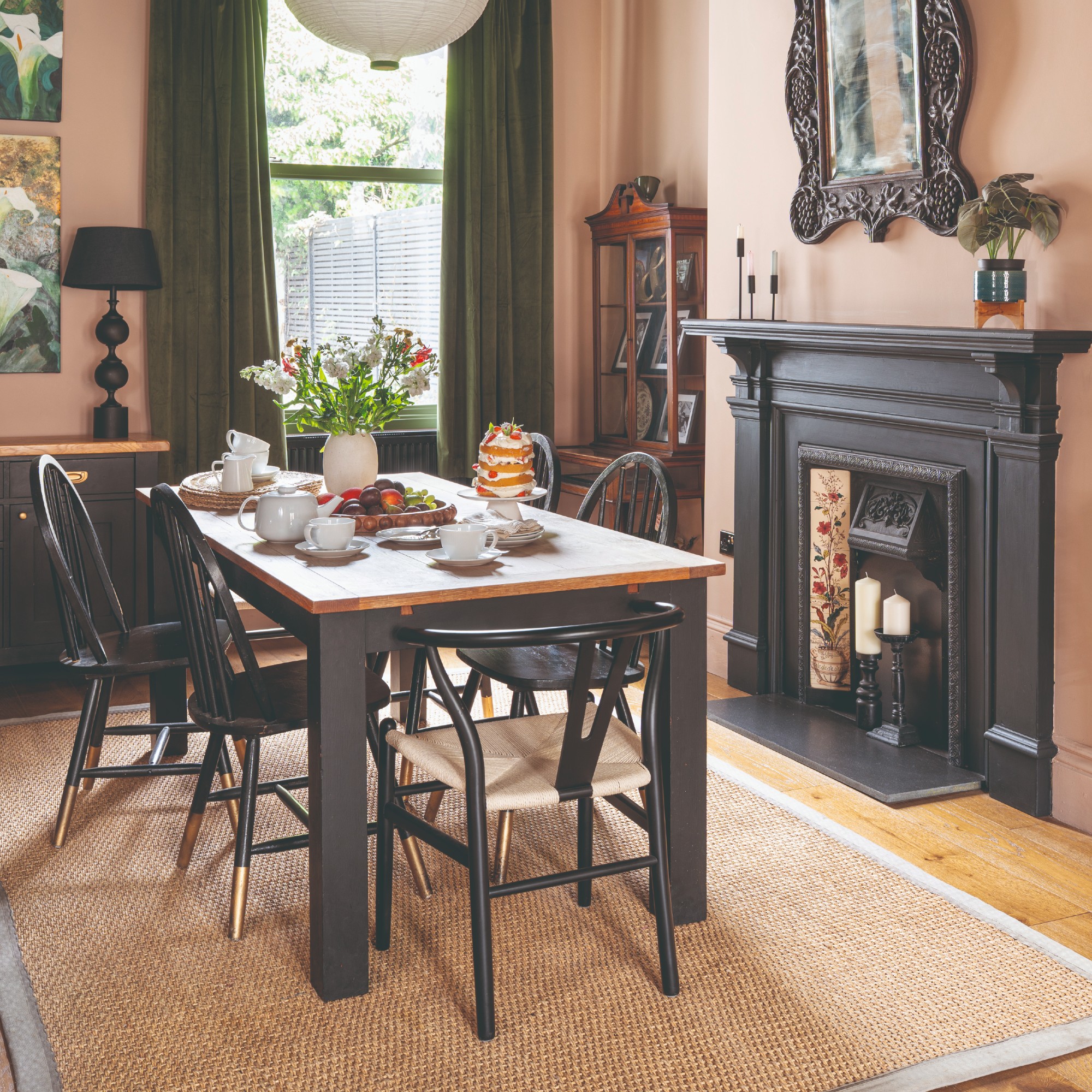A pink-painted dining room with a black wooden dining table and chairs and a jute rug underneath