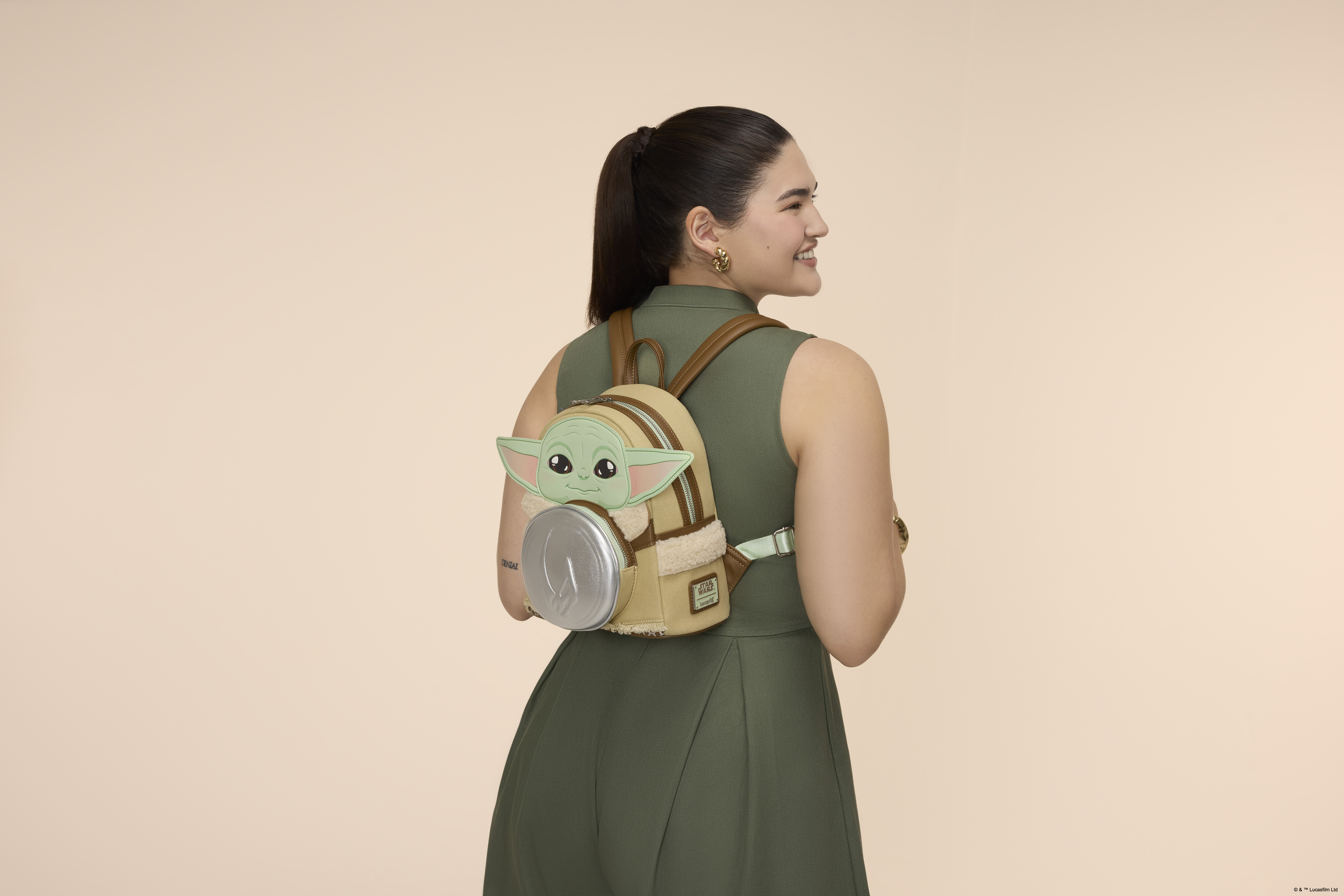 A woman wears a Grogu Loungefly mini-backpack in a pink environment