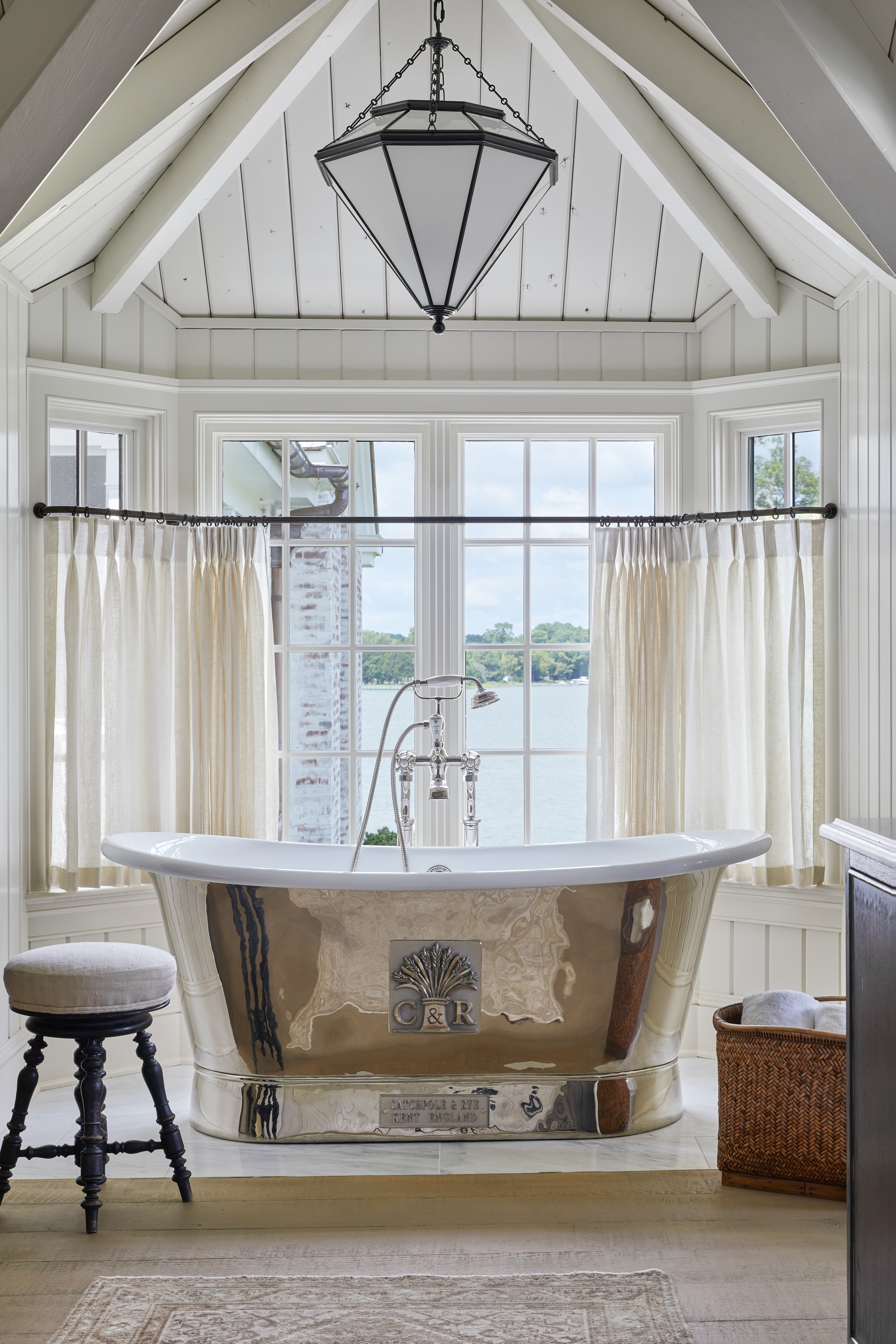 Bright, sunlit bathroom with a thatched ceiling and large windows. A chrome shell motif bathtub sits in the center