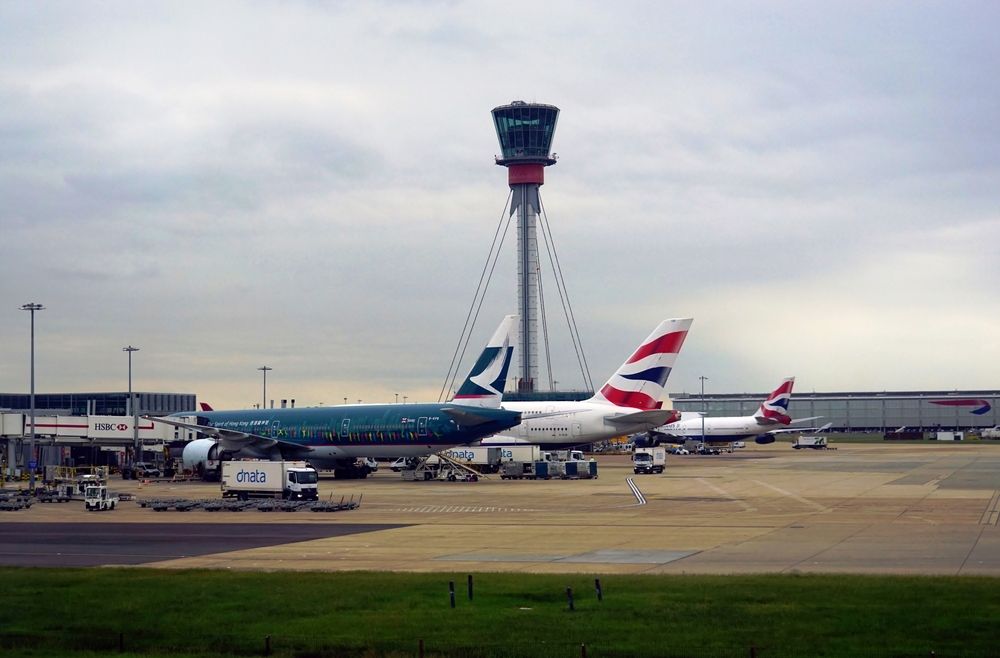 An airport scene with aircraft waiting at the terminal and the control tower visible in the distance.