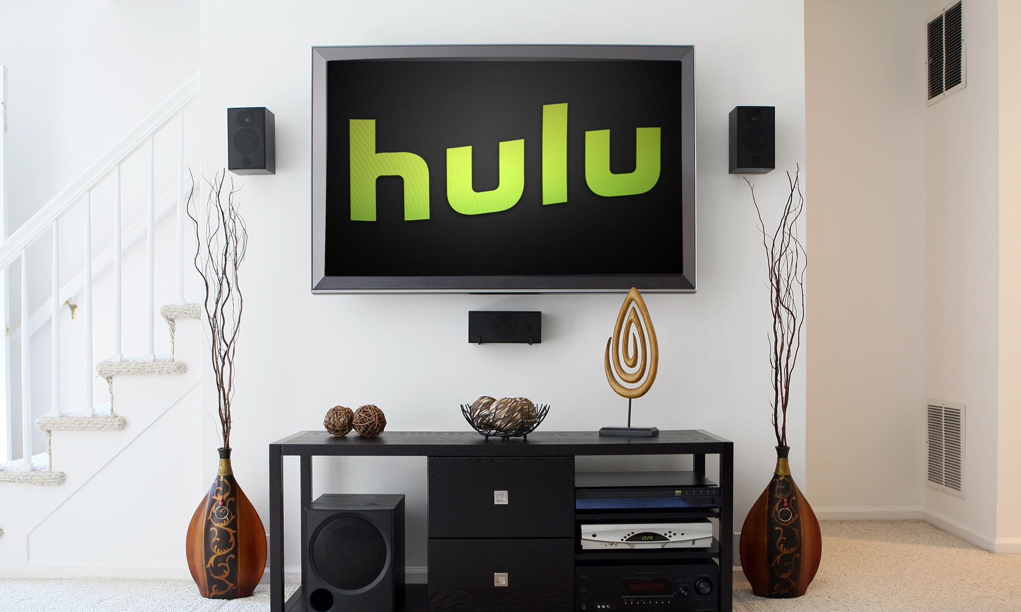Гостиная, на стене висит телевизор, на котором зелеными буквами написано «Hulu».  Под телевизором стоит тумба с украшениями.
