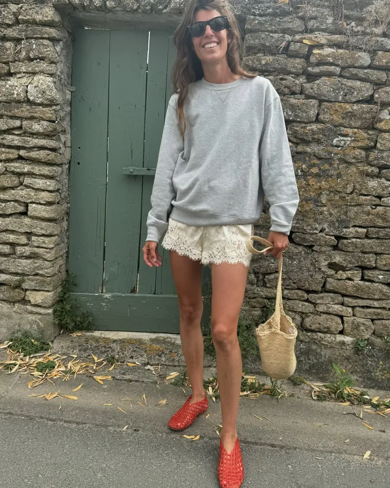 Woman in oversize gray sweatshirt, silk shorts, and red jelly shoes.