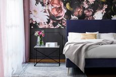 Floral mural in green bedroom with blue upholstered bed, grey throw and low pile rug