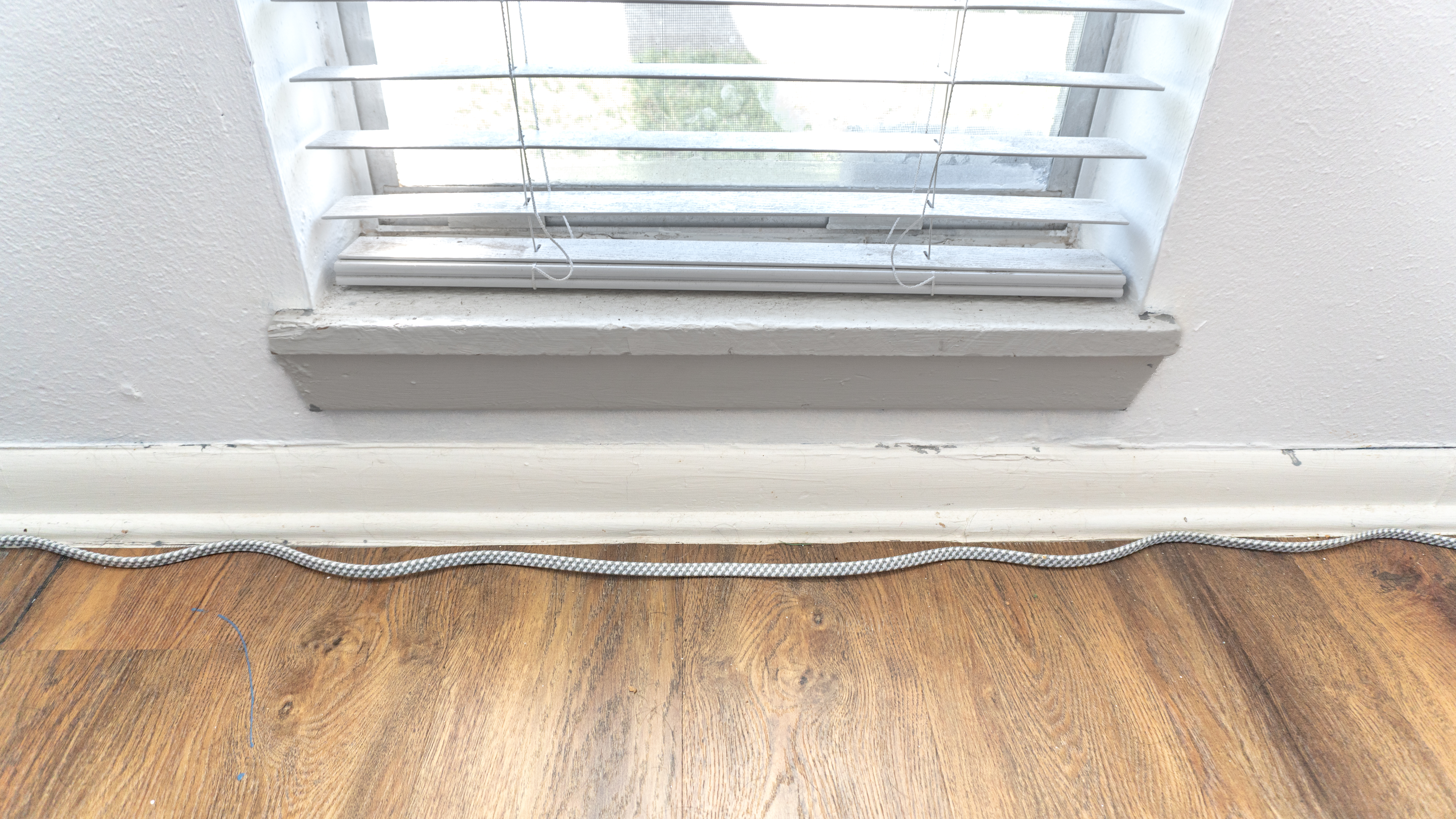 A braided cable from a surge protector with a bunch of kinks in it lying on the floor next to a window