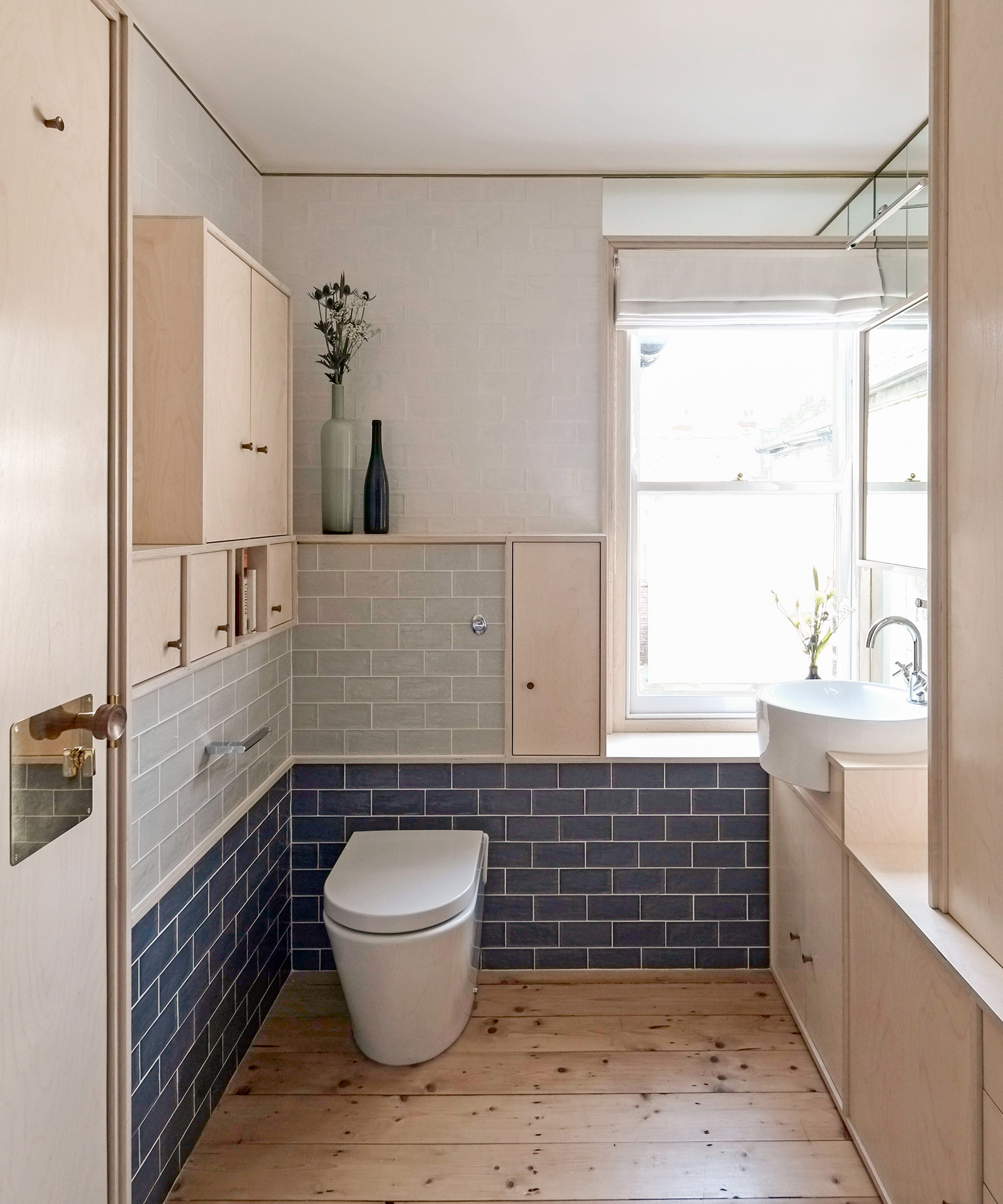 Small bathroom with two tones of blue bathroom tiles and birch plywood storage