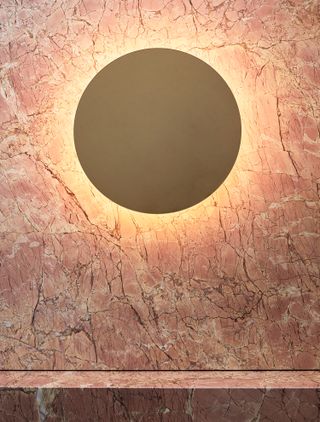 View of a pink marble wall and round backlit wall-mounted light in a changing room at Studio Warrior One