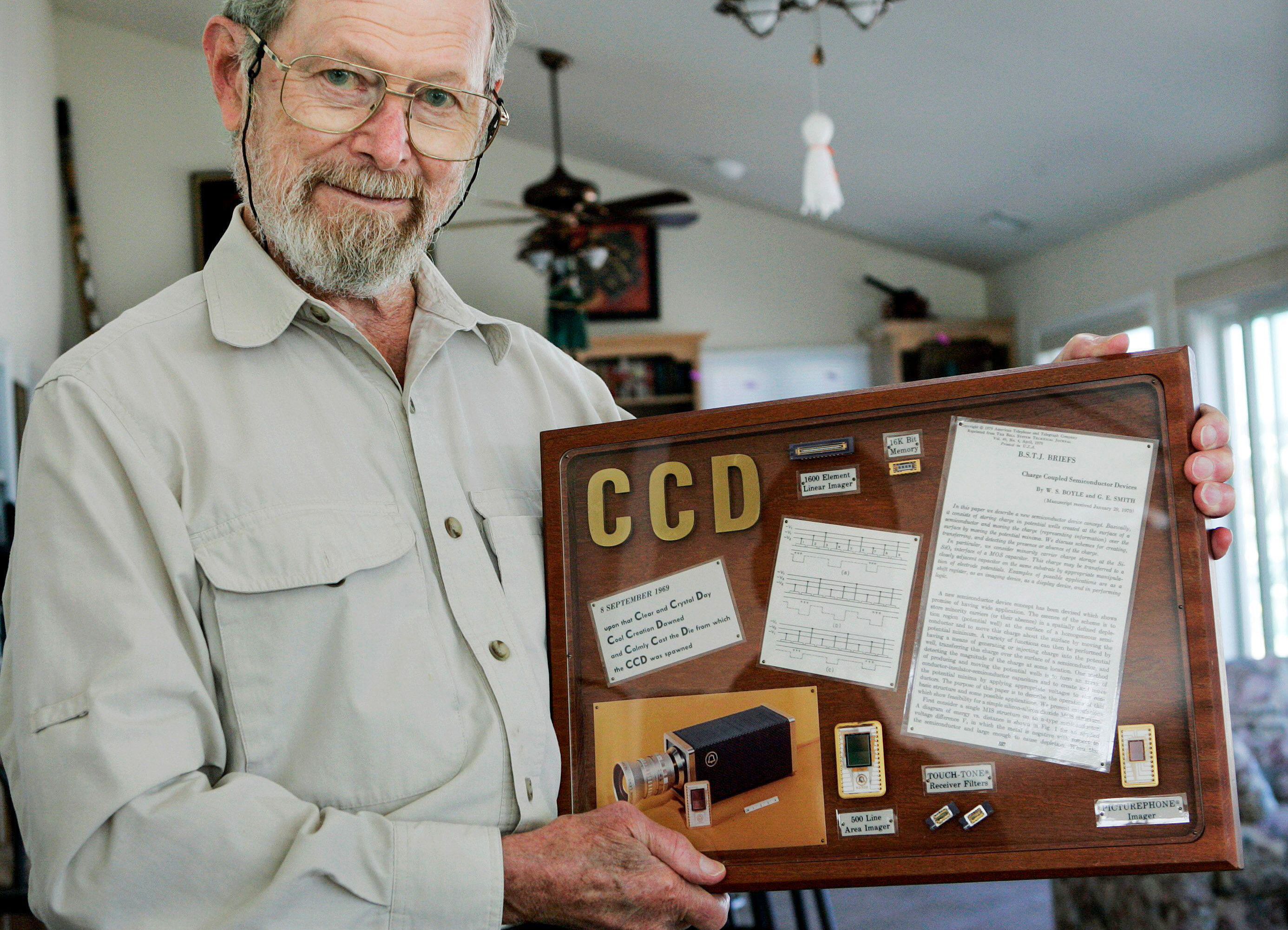 George E. Smith, 79, holds a display with a photograph of the first video telephone and some early CCD chips at his home in Waretown, N.J., Tuesday, Oct. 6, 2009, after it was announced that he had won the Nobel Prize in physics. Smith along with Willard S. Boyle, 85, were honored for inventing the eye of the digital camera, a sensor able to transform light into a large number of pixels, the tiny points of color that are the building blocks of every digital image. (AP Photo/Mel Evans)