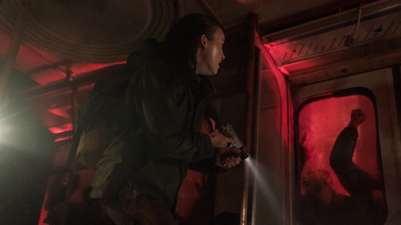 Ellie in subway car holding flashlight and gun while runners bang on window in The Last of Us Season 2 "Day One"