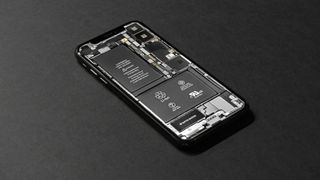 An iPhone sitting on a desk. Its back has been removed, exposing its internal compontents.