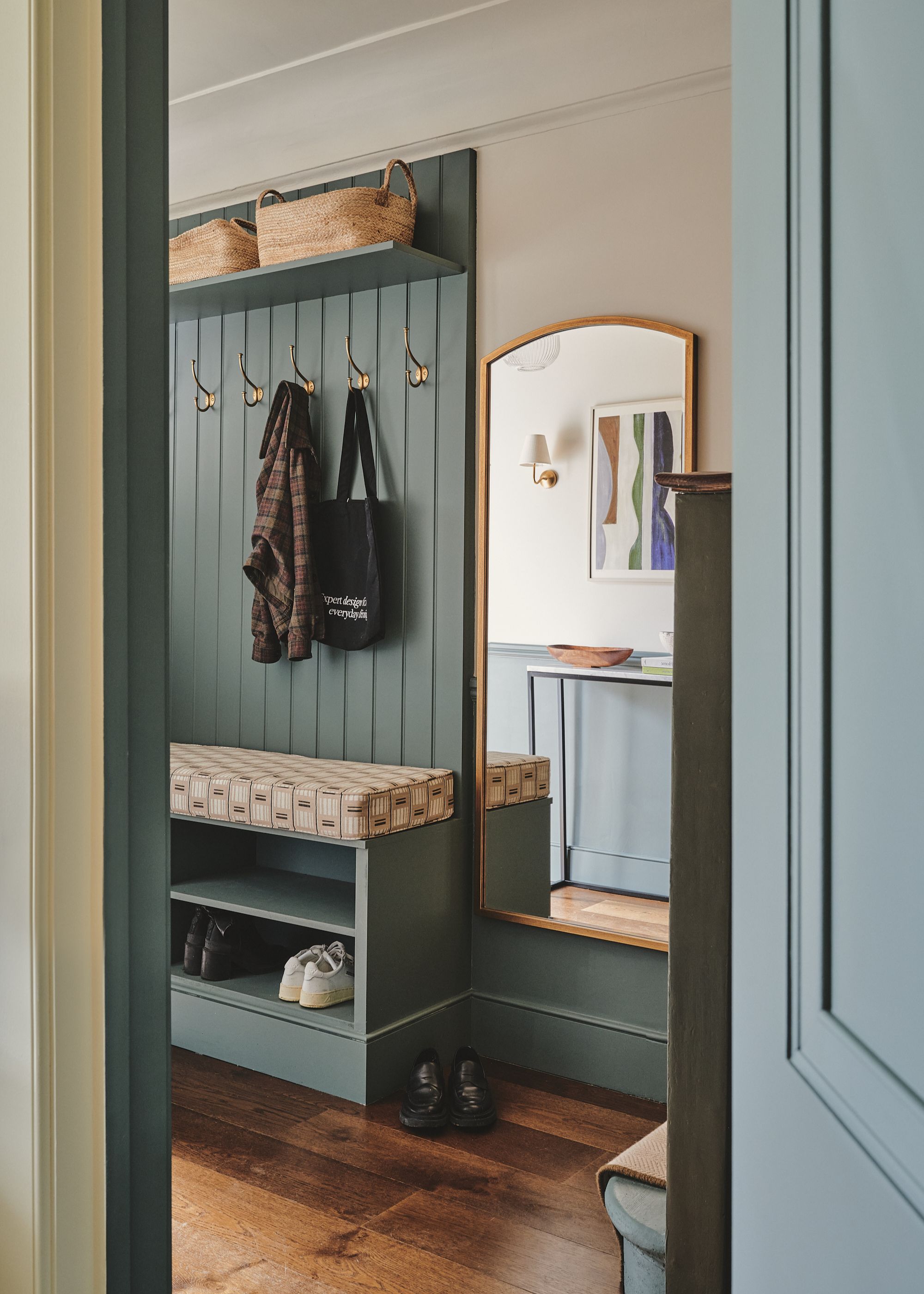 A blue entryway mud room with brass hooks, a bench, shoe storage, a wall mirror, and baskets