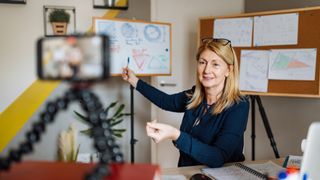 Teacher recording lesson pointing at whiteboard in background