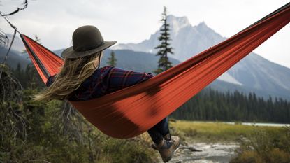 A woman relaxes in a hammock while looking at mountainous scenery.
