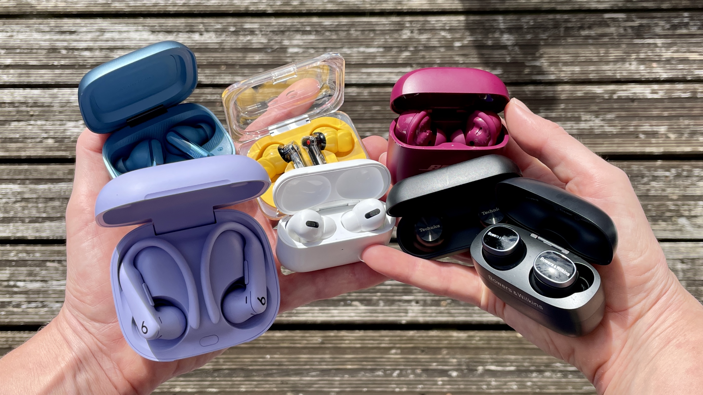 7 of our best noise-cancelling earbuds buys, held in two hands above a boardwalk 
