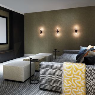 small media room with graphic print couch, 3 footstools, 3 wall lights, graphic carpet, textured wallpaper, cushions, yellow blanket, side tables