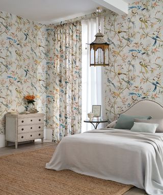 Large bedroom with matching floral patterned curtains and wallpaper, bed with upholstered headboard, hanging lantern light, natural textured rug