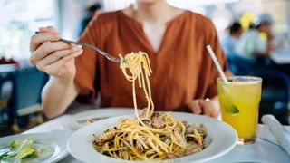 A close-up image of a woman eating a bowl of seafood pasta in a restaurant. 