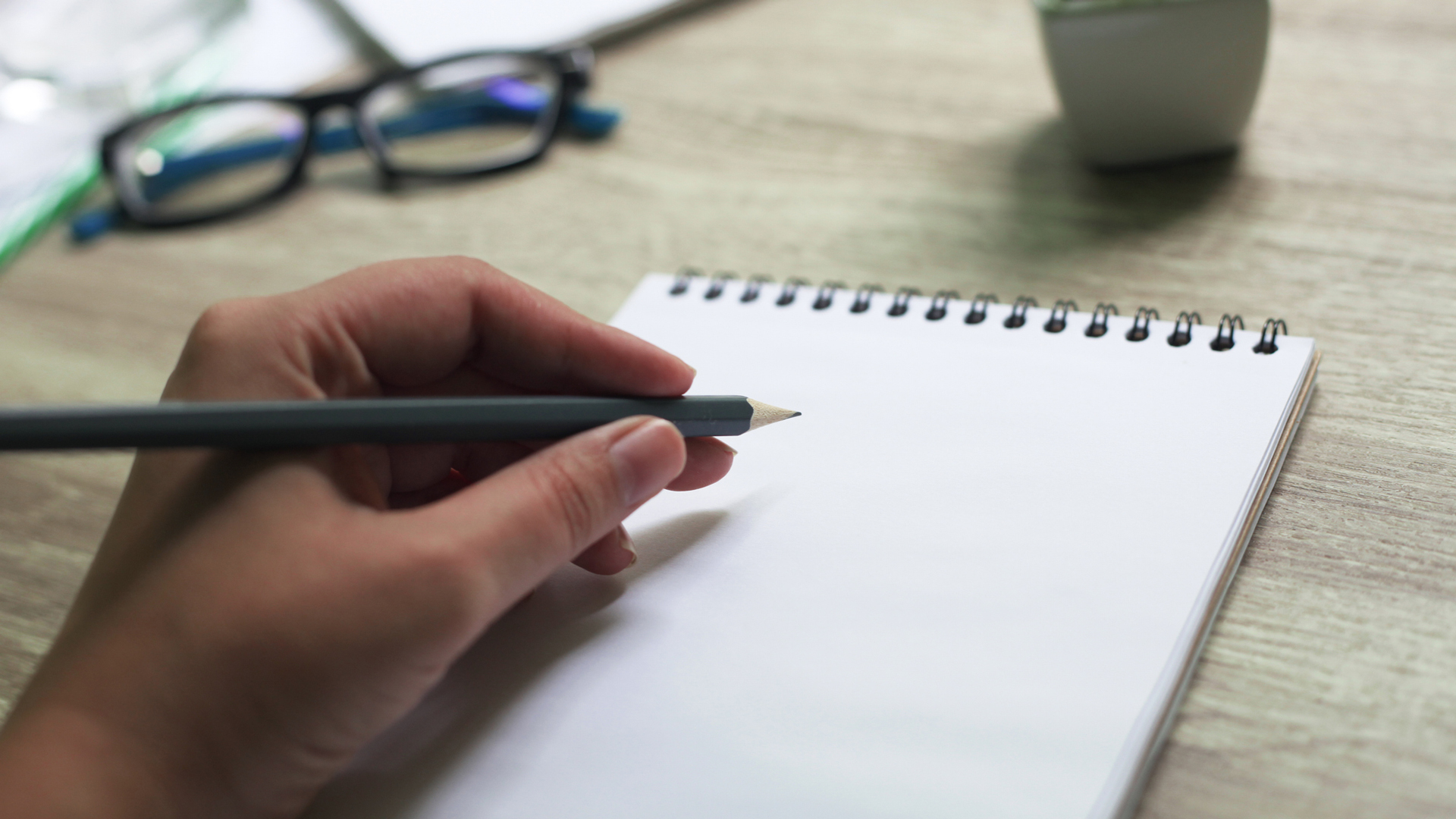 left handed person poised with a pencil on a notebook