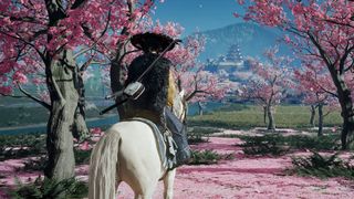 Ghost of Yotei gameplay showing Atsu sitting on her horse between bright pink cherry blossoms, looking at a distant fortification built against a mountain