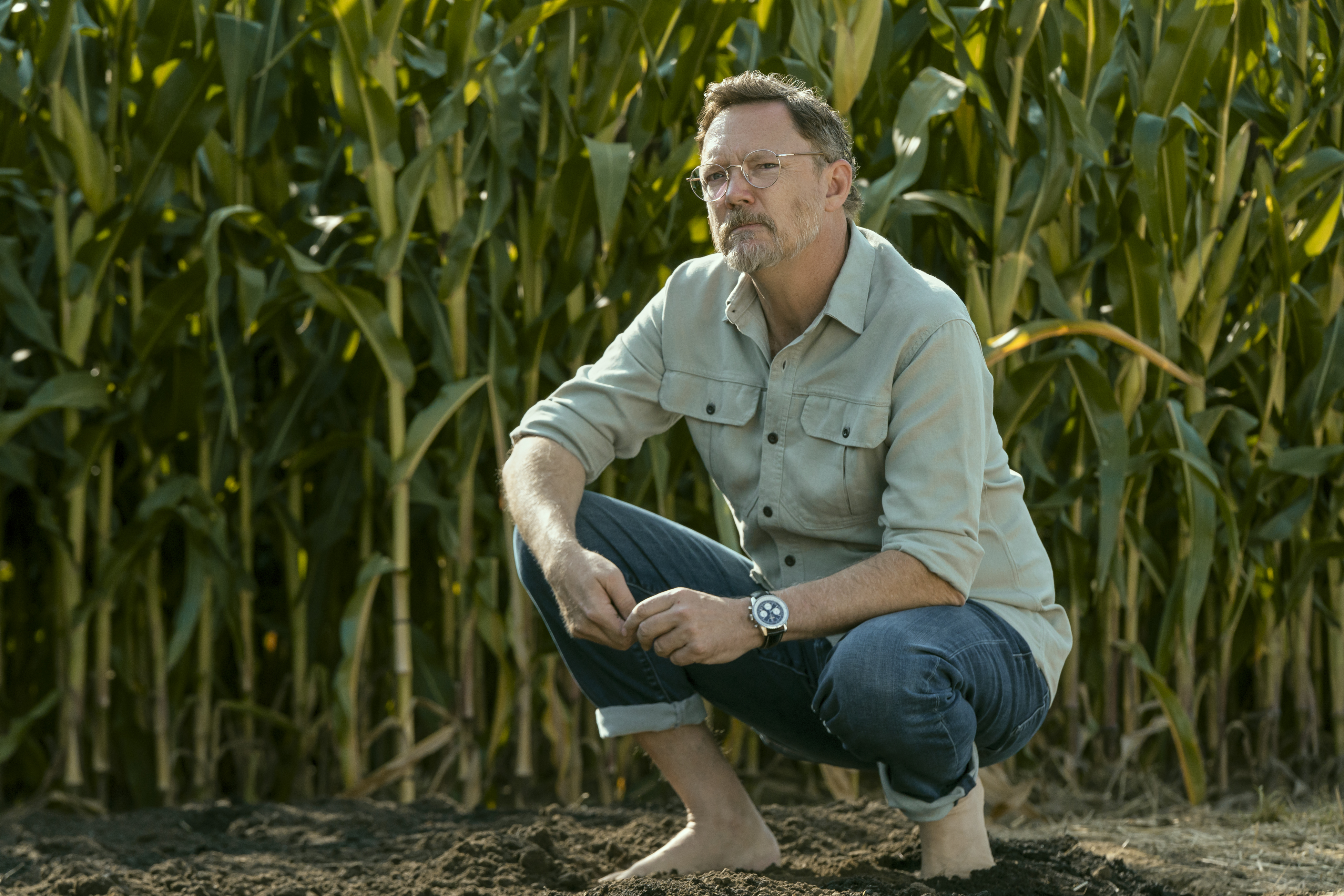 A still from 'Cross' season 2 of matthew lillard as lance durand without shoes on crouching in a corn field