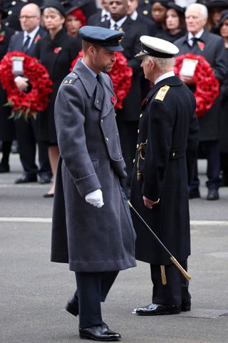 King Charles and Prince William wearing military uniforms walking away from each other in front of people holding red wreaths