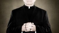 A faceless shot of a priest with his hands clasped, holding a rosary.