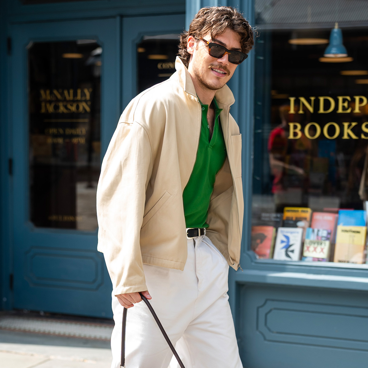 Jack Innanen is seen wearing a canvas jacket, green sweater, white pants, and a black belt.