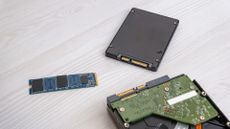 An M2 SSD drive placed near SATA SSD and opened hard disk drive on a light wooden desk.