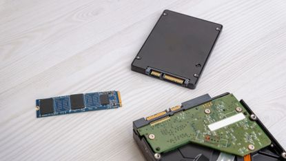 An M2 SSD drive placed near SATA SSD and opened hard disk drive on a light wooden desk.