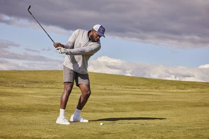 A man wearing Golf Apparel Shop attire teeing off on a hillside green