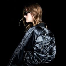 Model against a black background wearing an AllSaints coat